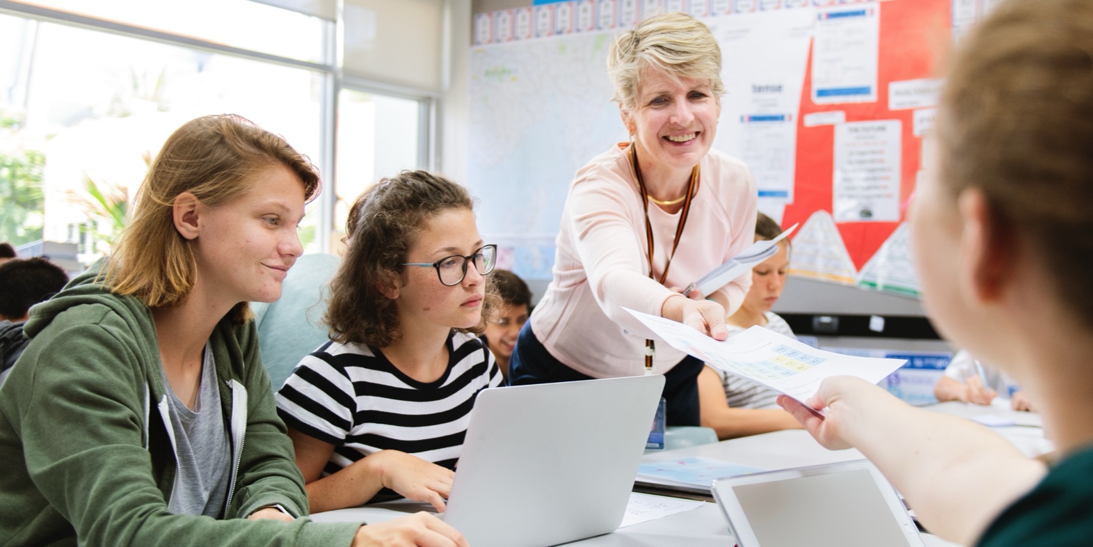 A smiling teacher handing back a sheet to her students