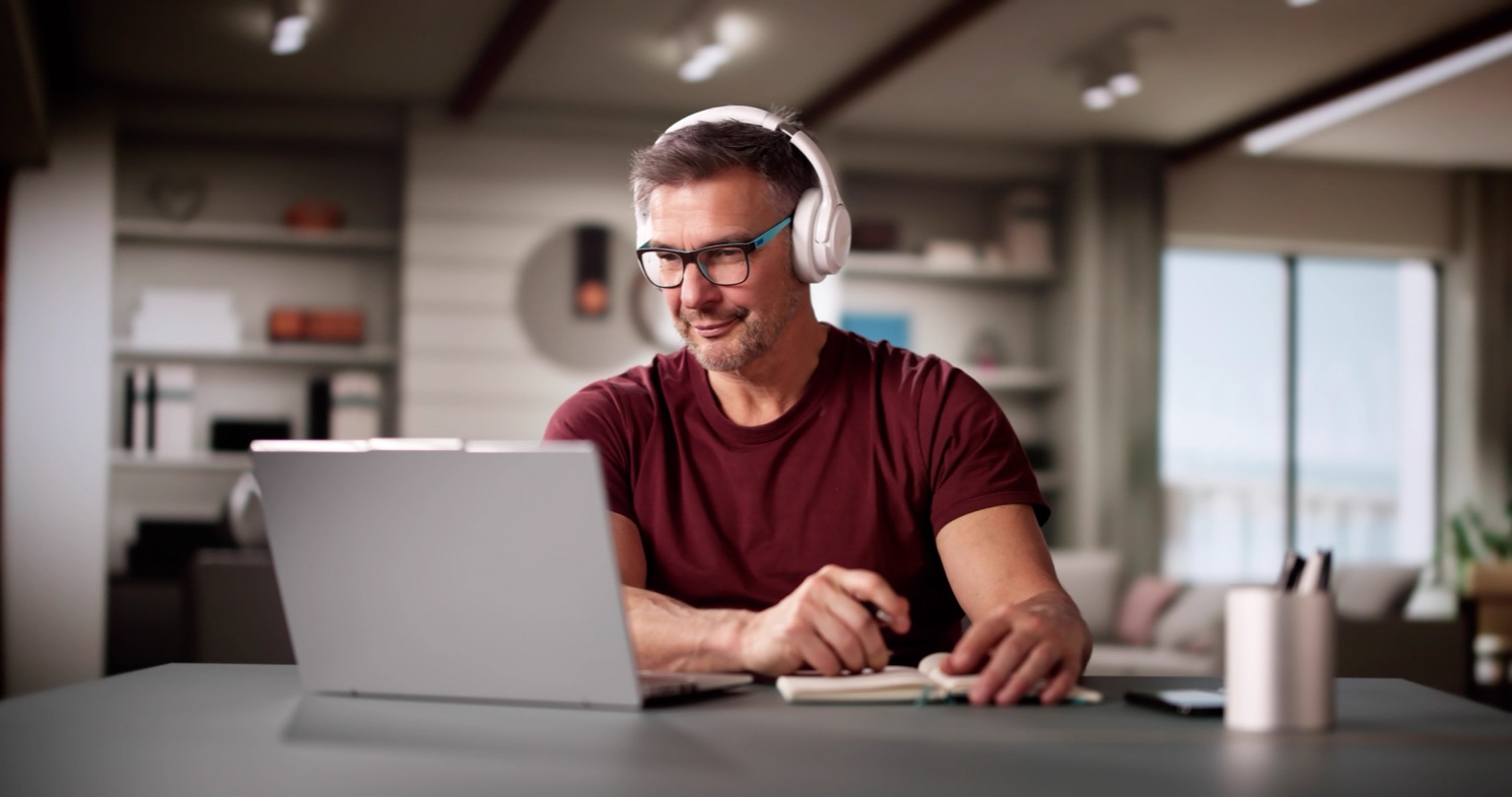 A teacher with headphones working on his laptop at home