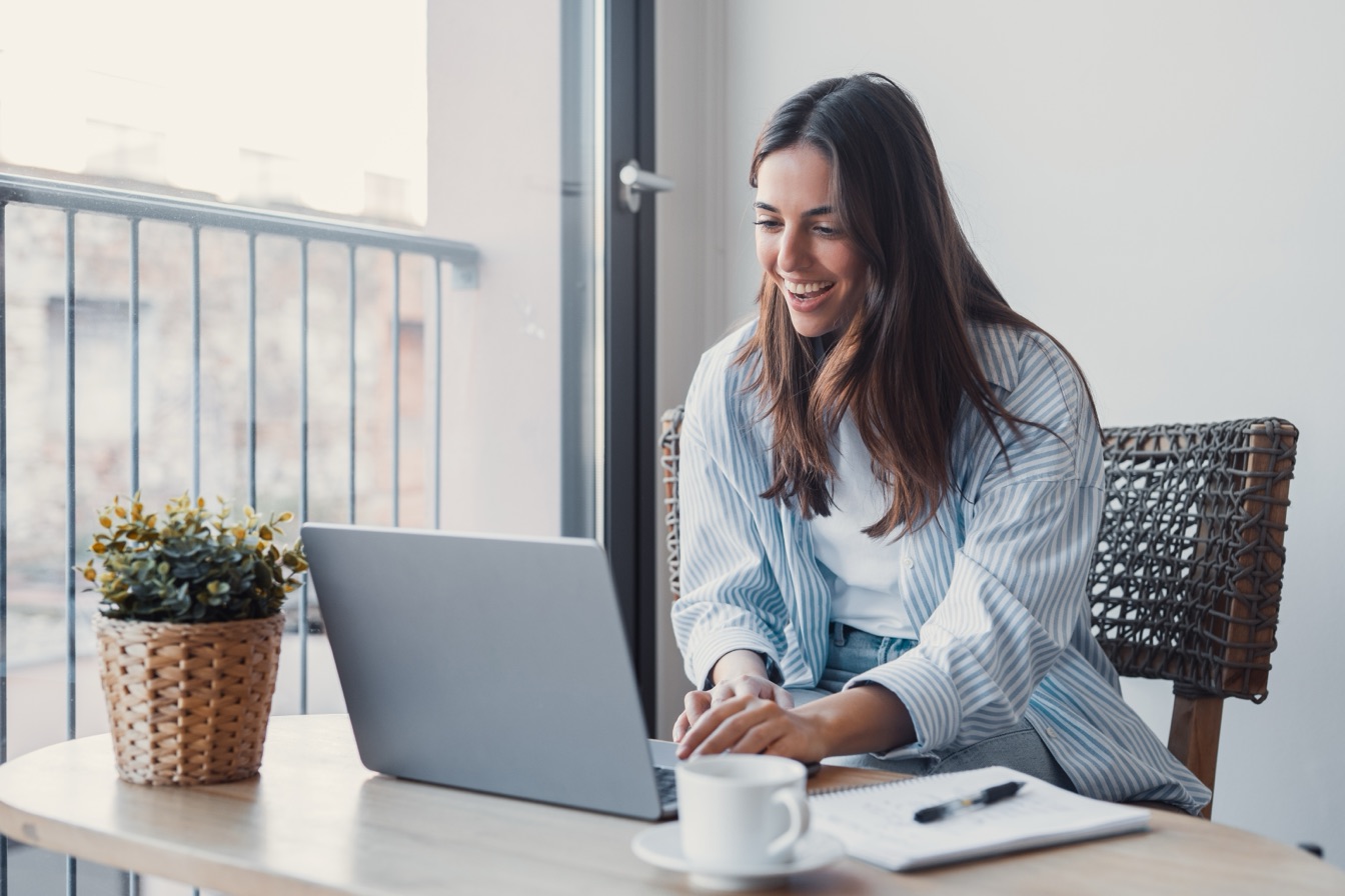 A smiling teacher working on a test on her laptop by the window